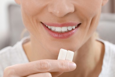Photo of Woman putting chewing gum pieces into mouth on blurred background, closeup