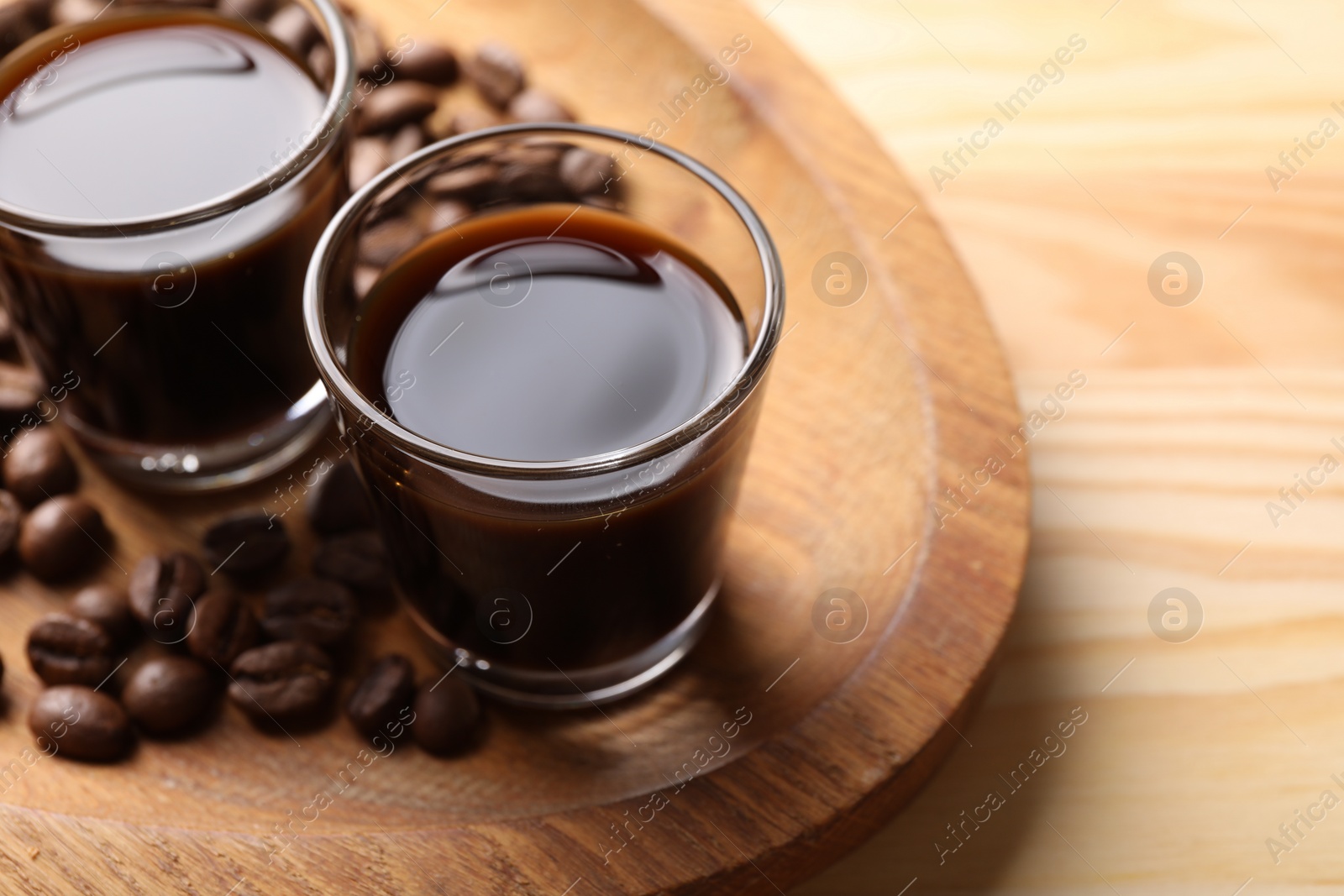 Photo of Shot glasses with coffee liqueur and beans on wooden table, closeup