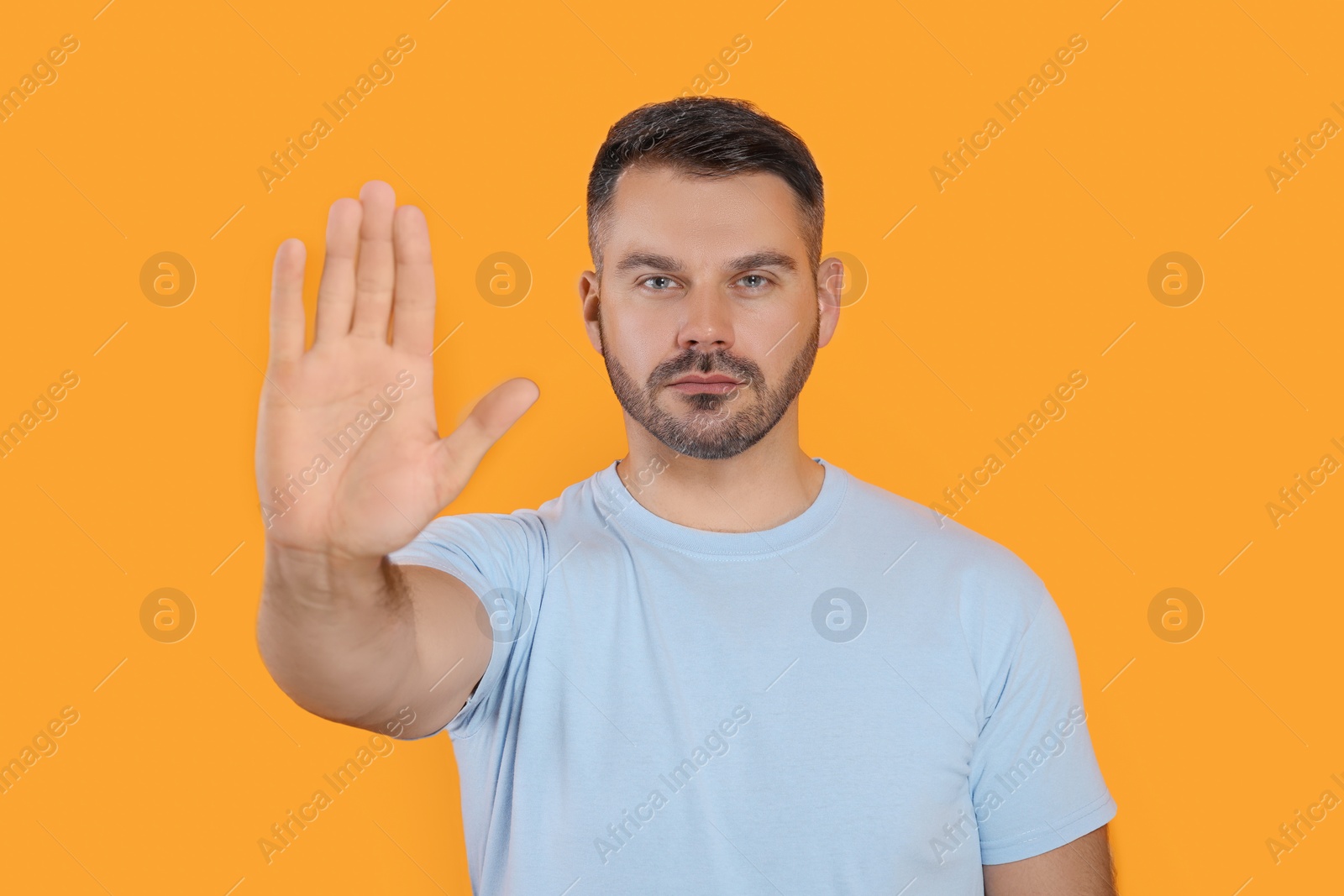 Photo of Handsome man showing stop gesture on orange background