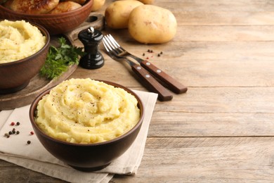 Photo of Bowl of tasty mashed potatoes with black pepper served on wooden table. Space for text