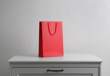 Photo of Paper shopping bag on white chest of drawers against light background