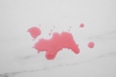 Photo of Puddle of red liquid on white marble surface, top view