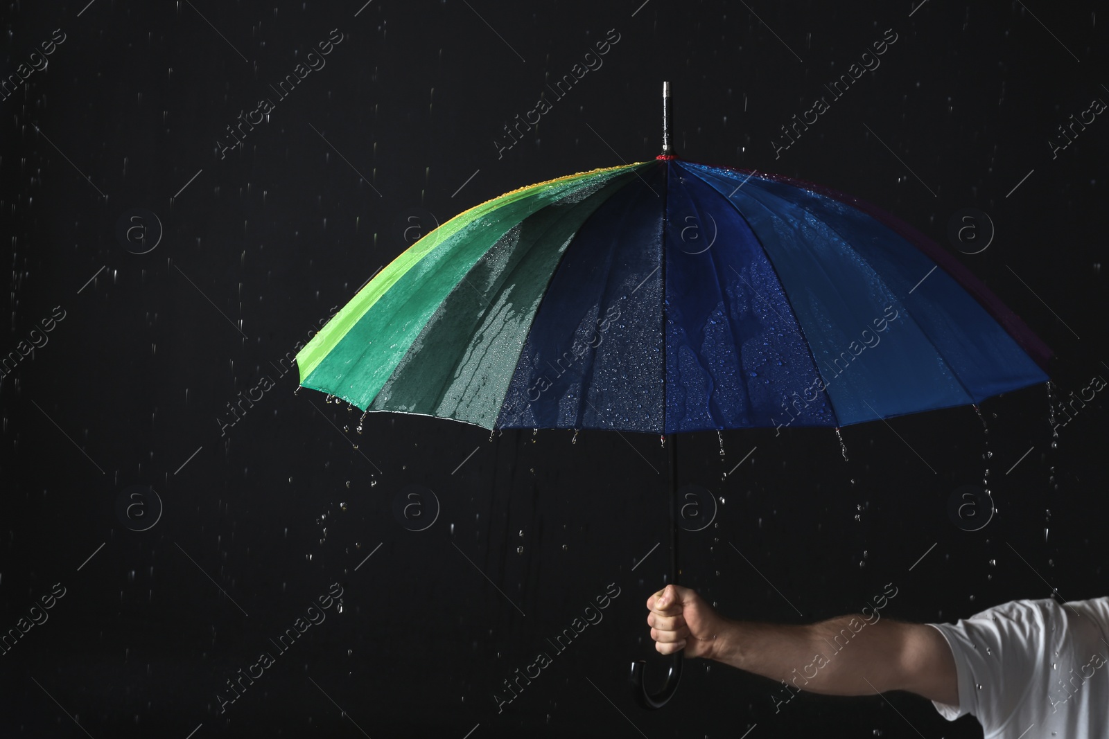 Photo of Man holding color umbrella under rain against black background, closeup