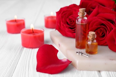 Photo of Bottles of love potion, red rose flowers, candles and small key on white wooden table, closeup