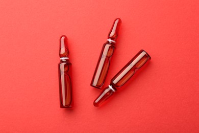 Photo of Glass ampoules with liquid on red background, top view