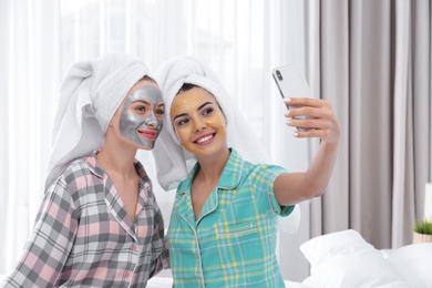 Photo of Young friends with facial masks taking selfie in bedroom at pamper party