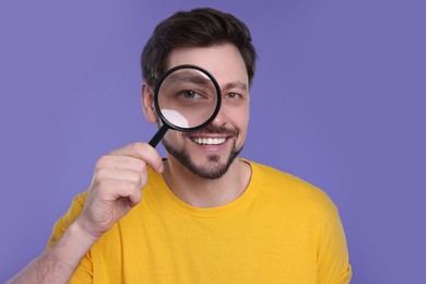 Photo of Happy man looking through magnifier glass on purple background