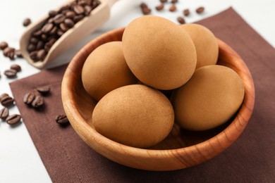 Easter eggs painted with natural dye in wooden bowl and coffee beans on table, closeup