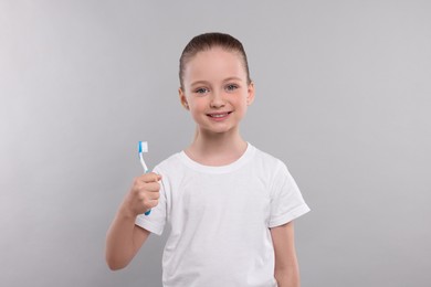 Photo of Happy girl holding toothbrush on light grey background