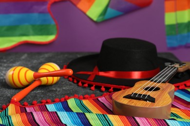 Photo of Black Flamenco hat, ukulele, poncho and maracas on dark table, closeup