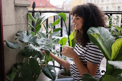Photo of Beautiful young woman spraying potted monstera with water on balcony