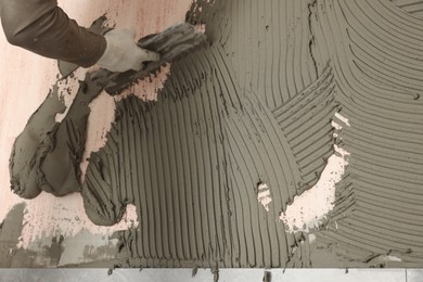 Photo of Worker applying cement on wall for tile installation, closeup