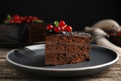 Photo of Piece of tasty homemade chocolate cake with berries and mint on wooden table, closeup