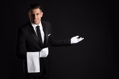 Handsome butler with towel on black background, space for text