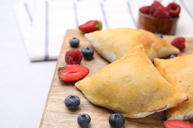 Photo of Wooden board with delicious samosas and berries on light table, closeup