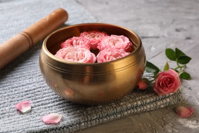 Tibetan singing bowl with water, beautiful roses and mallet on grey textured table