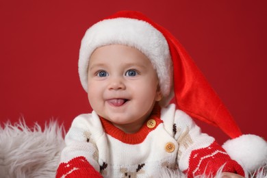 Cute baby in Santa hat on red background. Christmas celebration