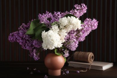 Photo of Beautiful lilac flowers in vase, twine and book on wooden table