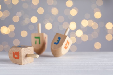 Photo of Hanukkah traditional dreidels on white wooden table against blurred lights. Space for text
