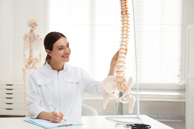 Female orthopedist at table near human spine model in office