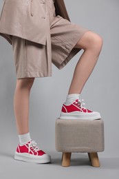 Photo of Woman posing in red classic old school sneakers and footstool on light gray background, closeup
