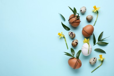 Photo of Easter eggs decorated with green leaves and flowers on light blue background, flat lay. Space for text