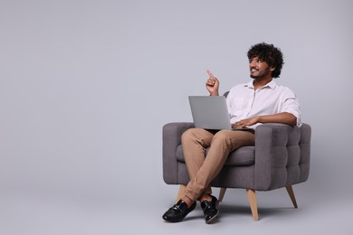 Photo of Smiling man with laptop sitting in armchair on light grey background, space for text