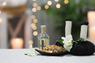 Photo of Spa composition. Herbal massage bags, essential oil and dry flowers on towel against blurred lights. Space for text