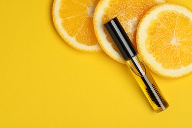 Photo of Tube of eyelash oil with fresh orange slices on yellow background, flat lay. Space for text