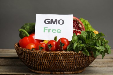 Photo of Tasty fresh GMO free products and paper card on wooden table against grey background