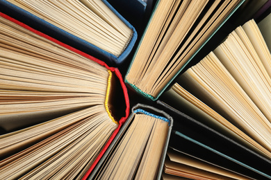 Photo of Many different hardcover books on dark background, top view