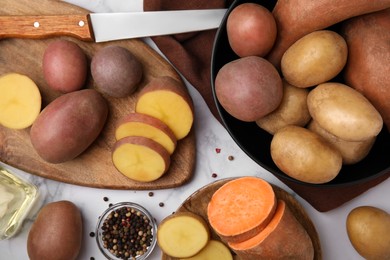 Photo of Different types of fresh potatoes on white marble table, flat lay
