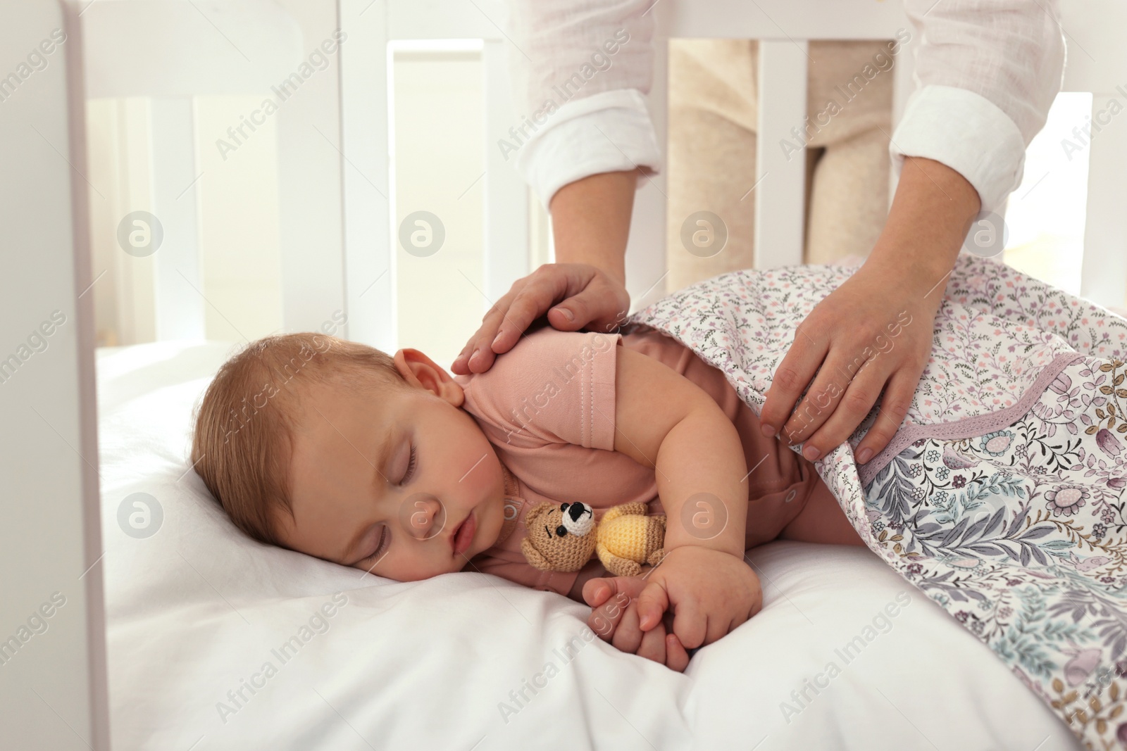 Photo of Mother covering her sleeping baby with blanket at home