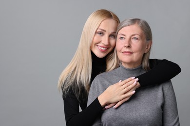 Family portrait of young woman and her mother on grey background. Space for text