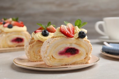 Photo of Pieces of tasty meringue roll with jam, cream, strawberry, blueberry and mint on light grey marble table, closeup