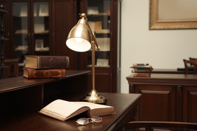 Photo of Books, glasses and lamp on wooden table in library reading room
