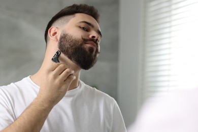 Photo of Handsome young man shaving with razor indoors. Space for text