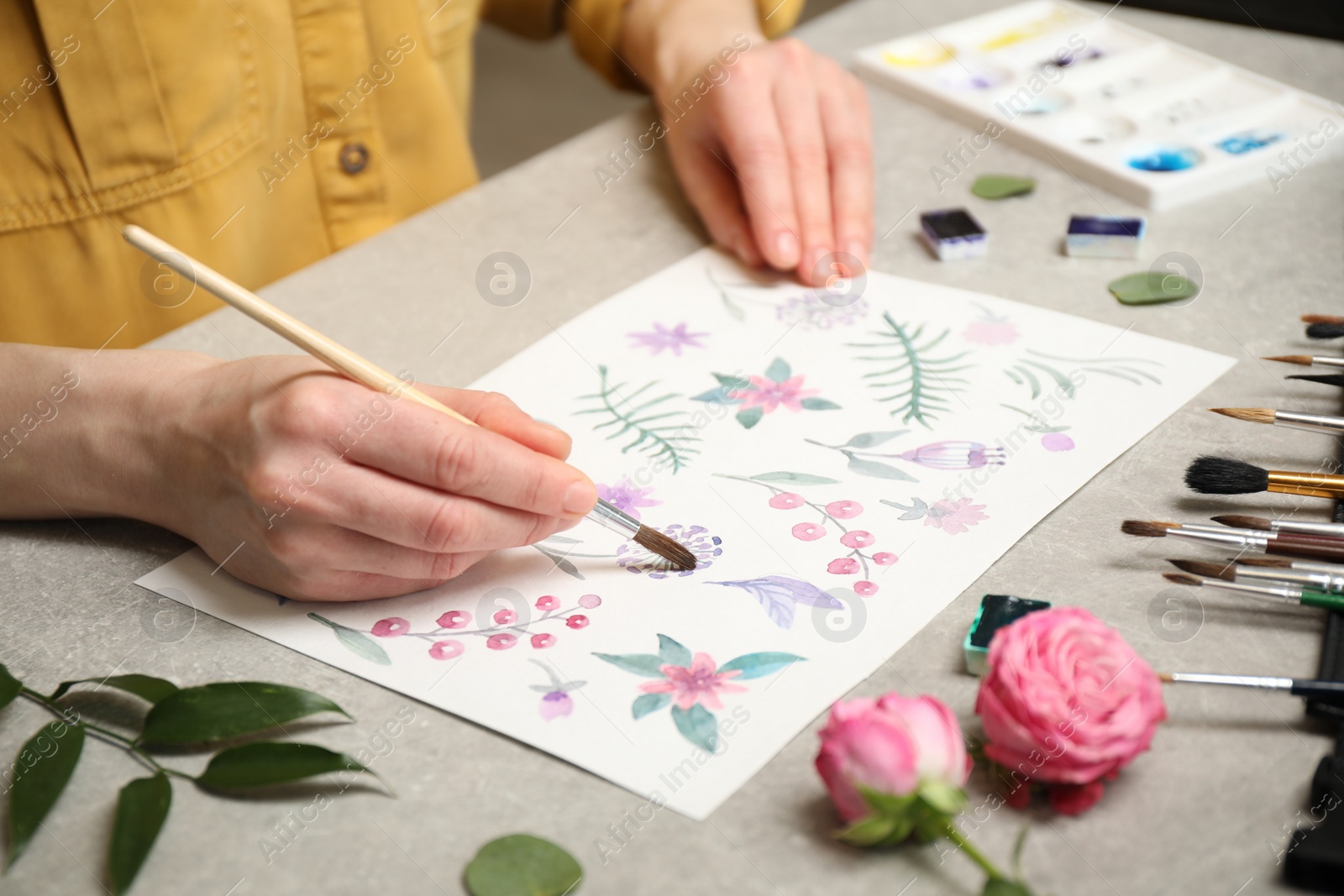 Photo of Woman painting flowers with watercolor at grey stone table, closeup