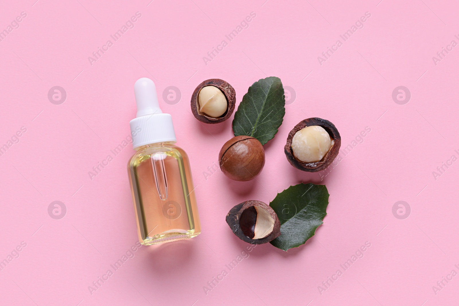 Photo of Delicious organic Macadamia nuts, natural oil and green leaves on pink background, flat lay