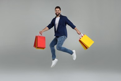 Photo of Happy man with many paper shopping bags jumping on grey background