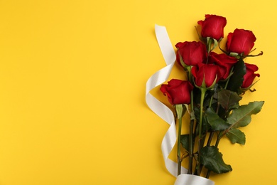 Photo of Beautiful red roses with white ribbon and space for text on yellow background, top view. Valentine's Day celebration