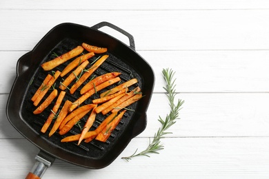 Photo of Grill pan with sweet potato fries on wooden background, top view. Space for text