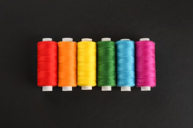 Photo of Different colorful sewing threads on black background, flat lay