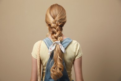Photo of Young woman with stylish bandana on beige background, back view