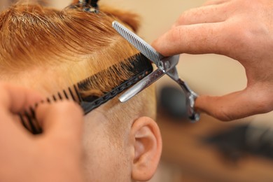 Photo of Professional hairdresser cutting boy's hair in beauty salon, closeup