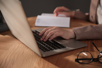 Photo of Woman working with laptop at wooden desk indoors, closeup