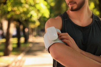 Photo of Man checking blood pressure with modern monitor after training in park on sunny day, closeup. Space for text