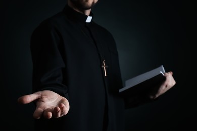 Photo of Priest with Bible praying on dark background, closeup