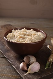 Photo of Spicy horseradish sauce in bowl and garlic on wooden table