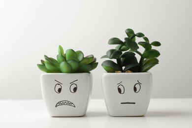 Photo of Beautiful potted houseplants with angry and concerned faces on white table. Emotional management